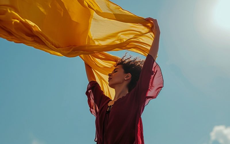 在风中举着黄色围巾的红色女性-AI工具研究所